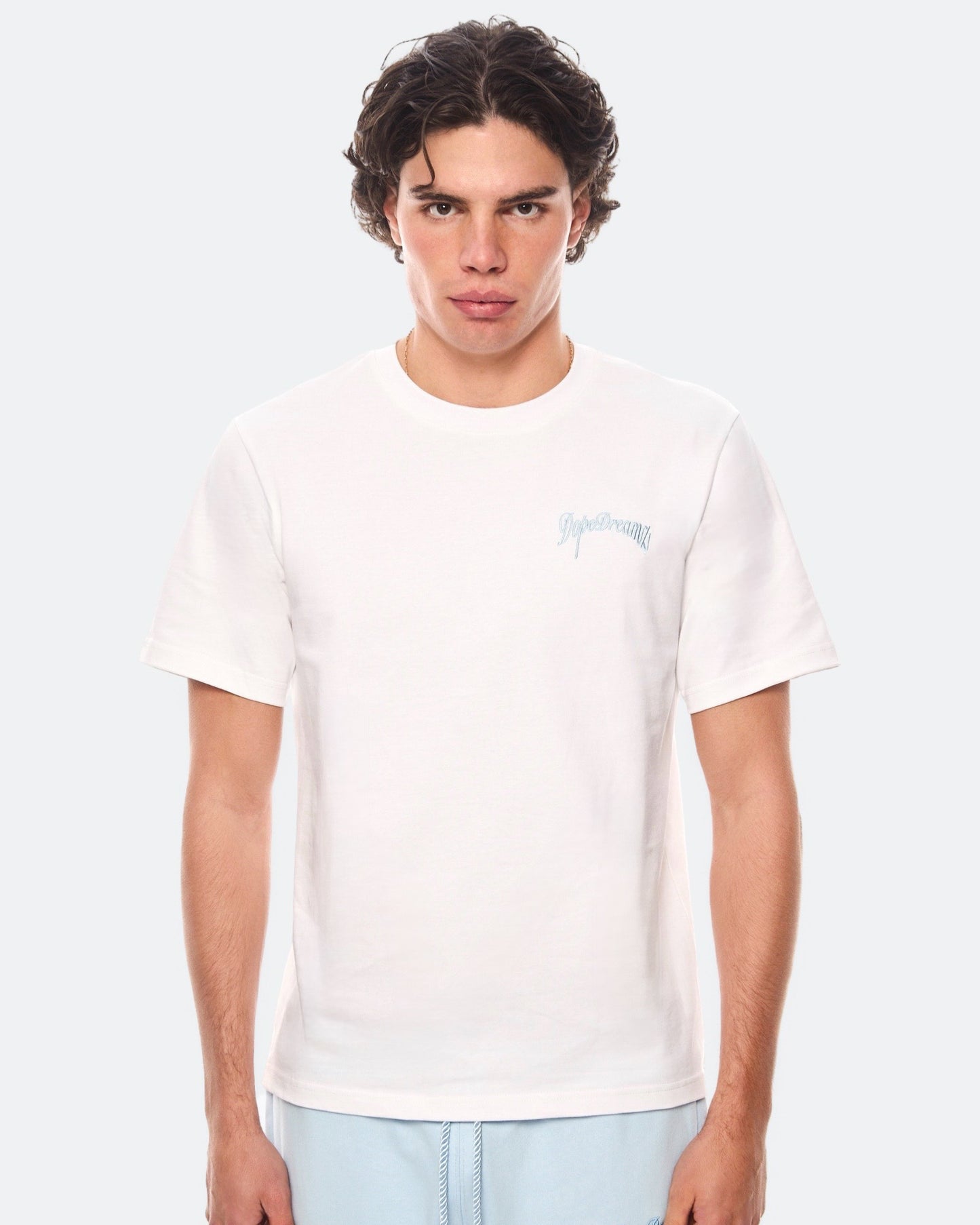 Model wearing white DopeDreamz t-shirt with blue 3D embroidered chest logo, front view
