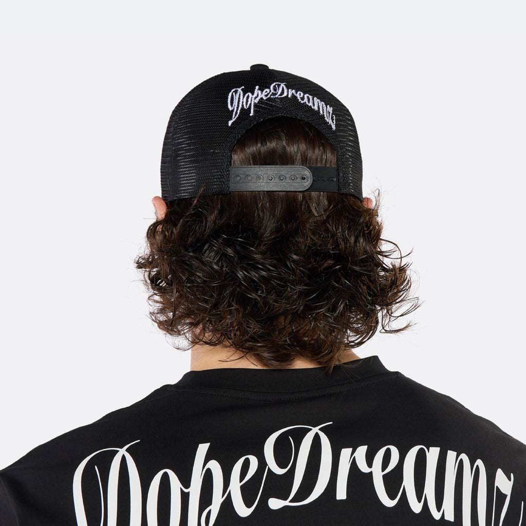 Close-up of a male model wearing the DopeDreamz Interlude Noir black trucker cap featuring a premium white embroidered DDZ monogram, paired with the matching black T-shirt featuring a tonal black embroidered DDZ monogram.