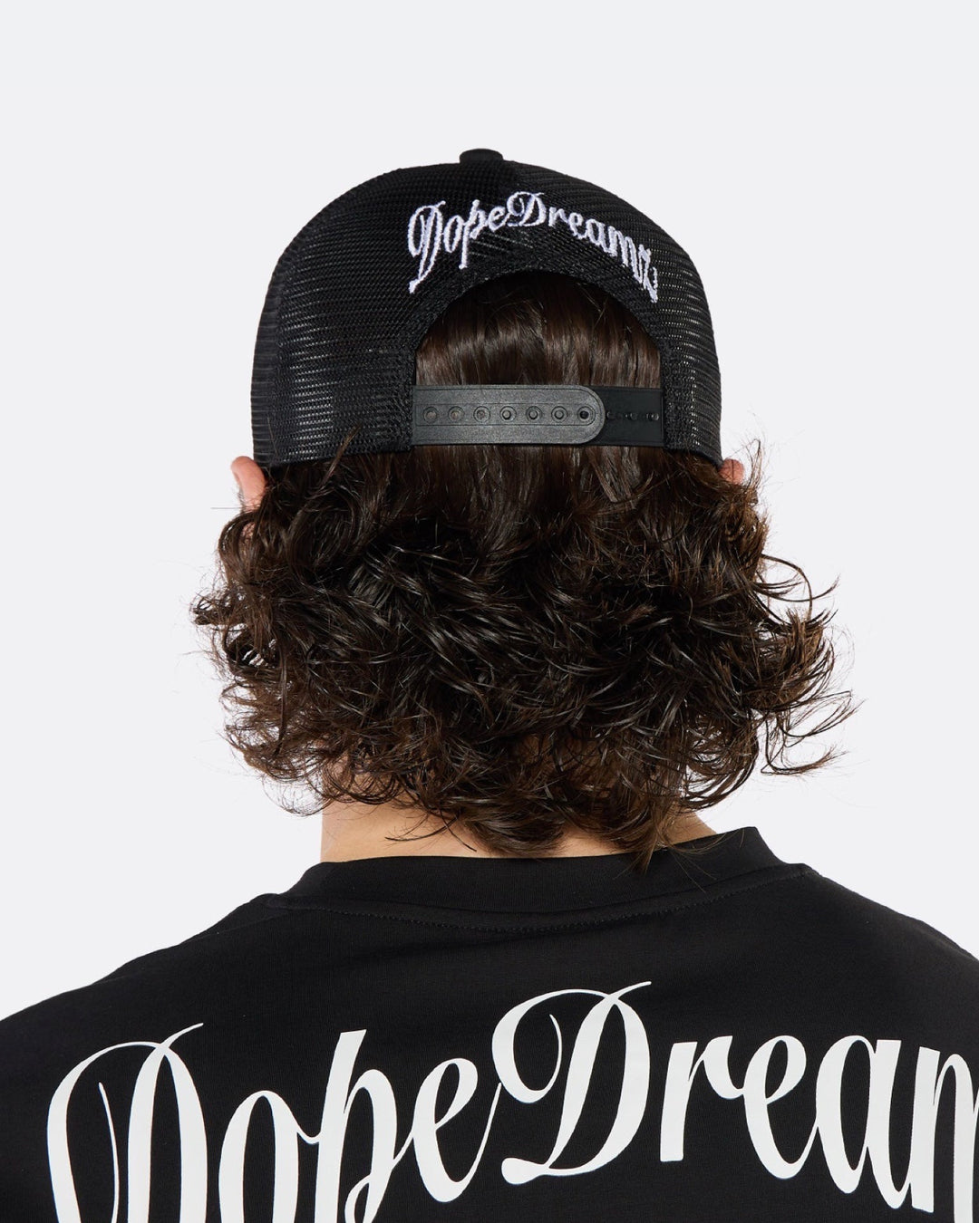 Close-up of a male model wearing the DopeDreamz Interlude Noir black trucker cap featuring a premium white embroidered DDZ monogram, paired with the matching black T-shirt featuring a tonal black embroidered DDZ monogram.