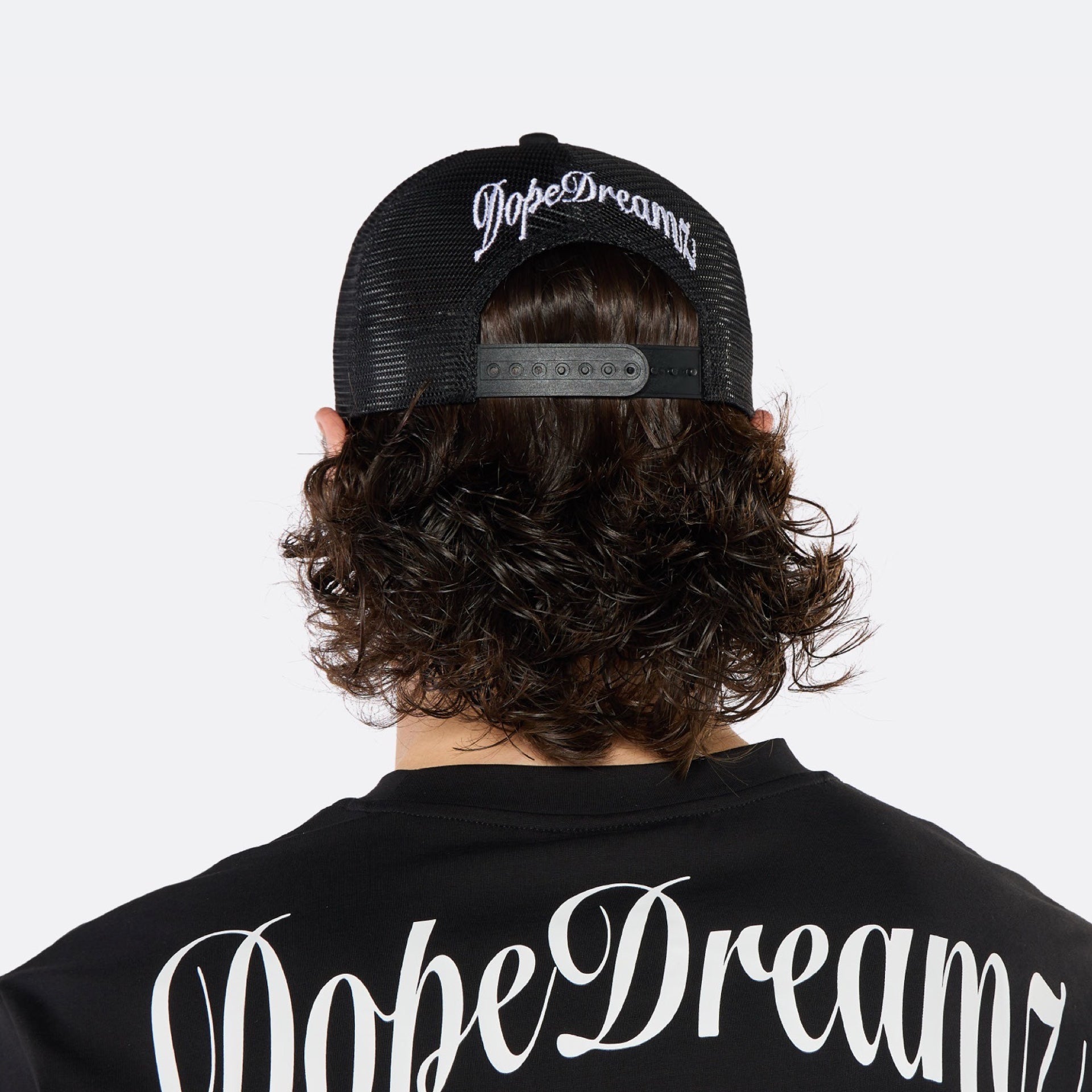 Close-up of a male model wearing the DopeDreamz Interlude Noir black trucker cap featuring a premium white embroidered DDZ monogram, paired with the matching black T-shirt featuring a tonal black embroidered DDZ monogram.