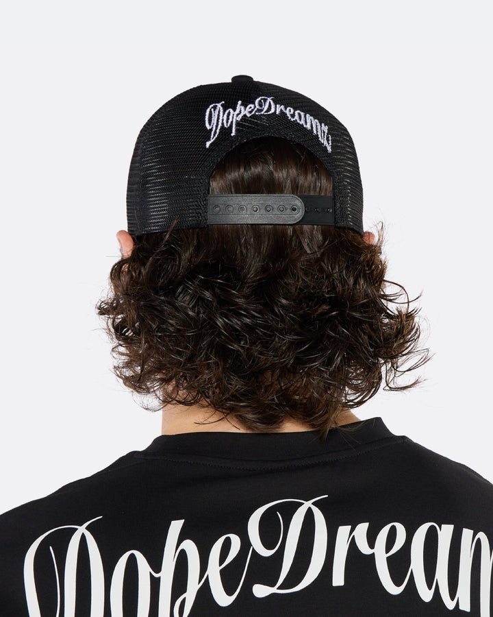 Close-up of a male model wearing the DopeDreamz Interlude Noir black trucker cap featuring a premium white embroidered DDZ monogram, paired with the matching black T-shirt featuring a tonal black embroidered DDZ monogram.