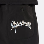 Close-up of the DopeDreamz Interlude Noir black premium shorts featuring the white embroidered DopeDreamz back pocket graphic and tonal DDZ metal button.