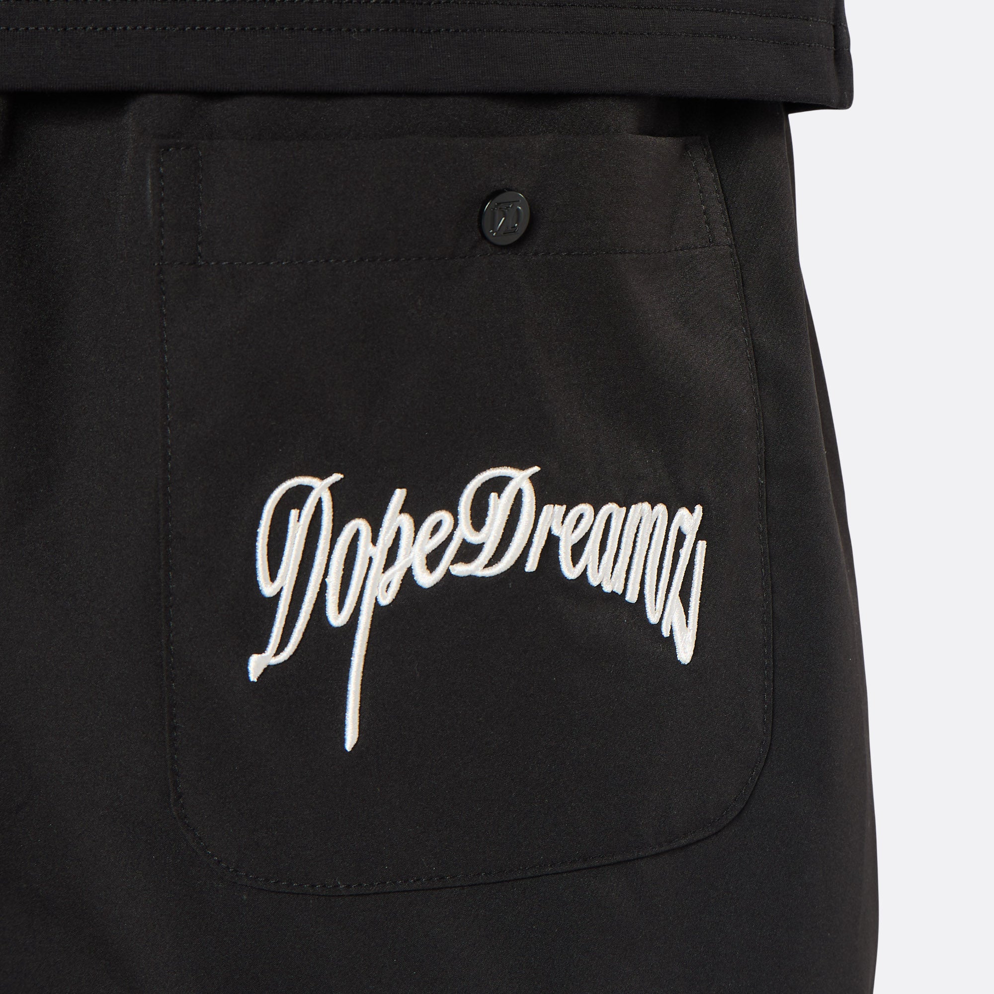 Close-up of the DopeDreamz Interlude Noir black premium shorts featuring the white embroidered DopeDreamz back pocket graphic and tonal DDZ metal button.