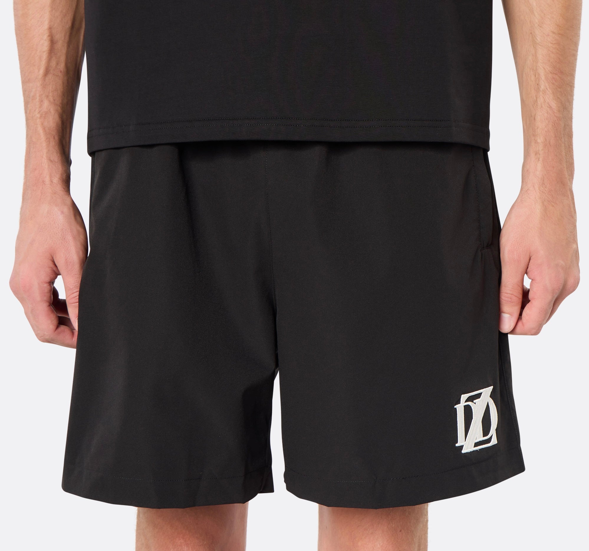 Close-up of a male model wearing the DopeDreamz Interlude Noir black premium shorts with white embroidered DDZ logo.