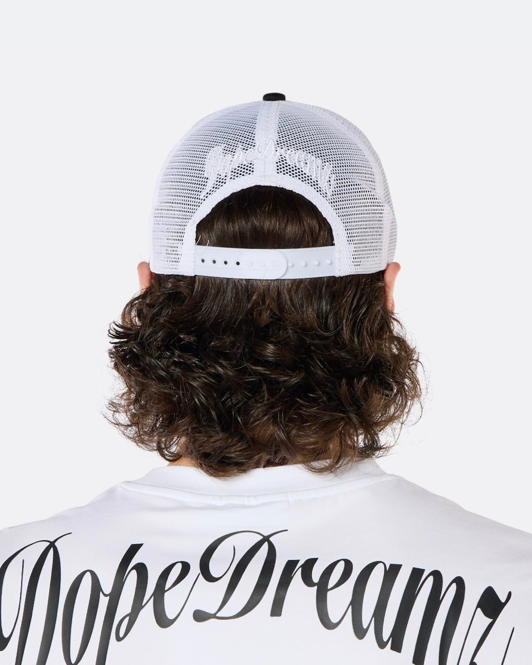 Close-up back view of a male model wearing the DopeDreamz Interlude Noir black and white trucker cap with white embroidered DopeDreamz rear logo.