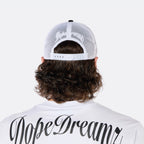 Close-up back view of a male model wearing the DopeDreamz Interlude Noir black and white trucker cap with white embroidered DopeDreamz rear logo.