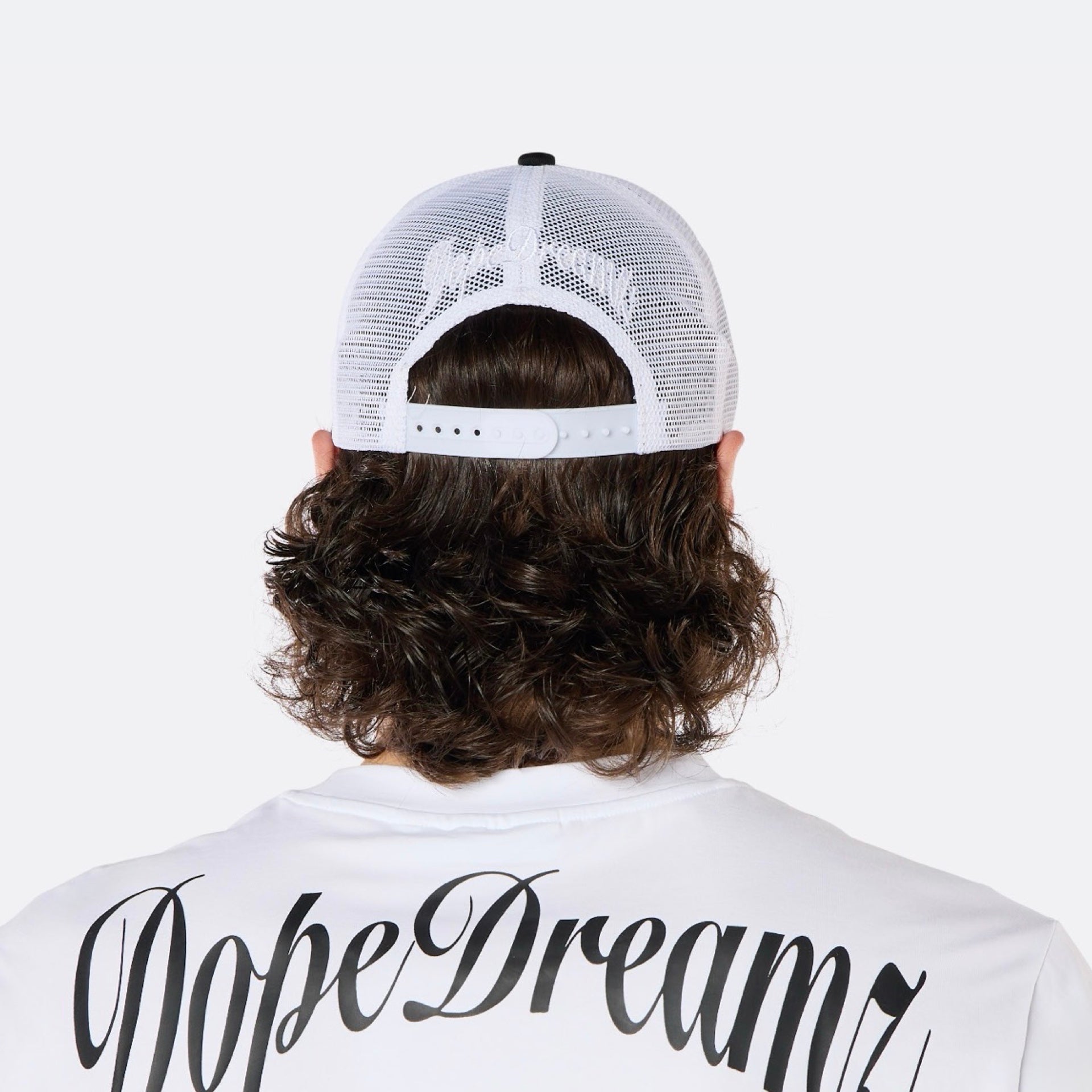 Close-up back view of a male model wearing the DopeDreamz Interlude Noir black and white trucker cap with white embroidered DopeDreamz rear logo.