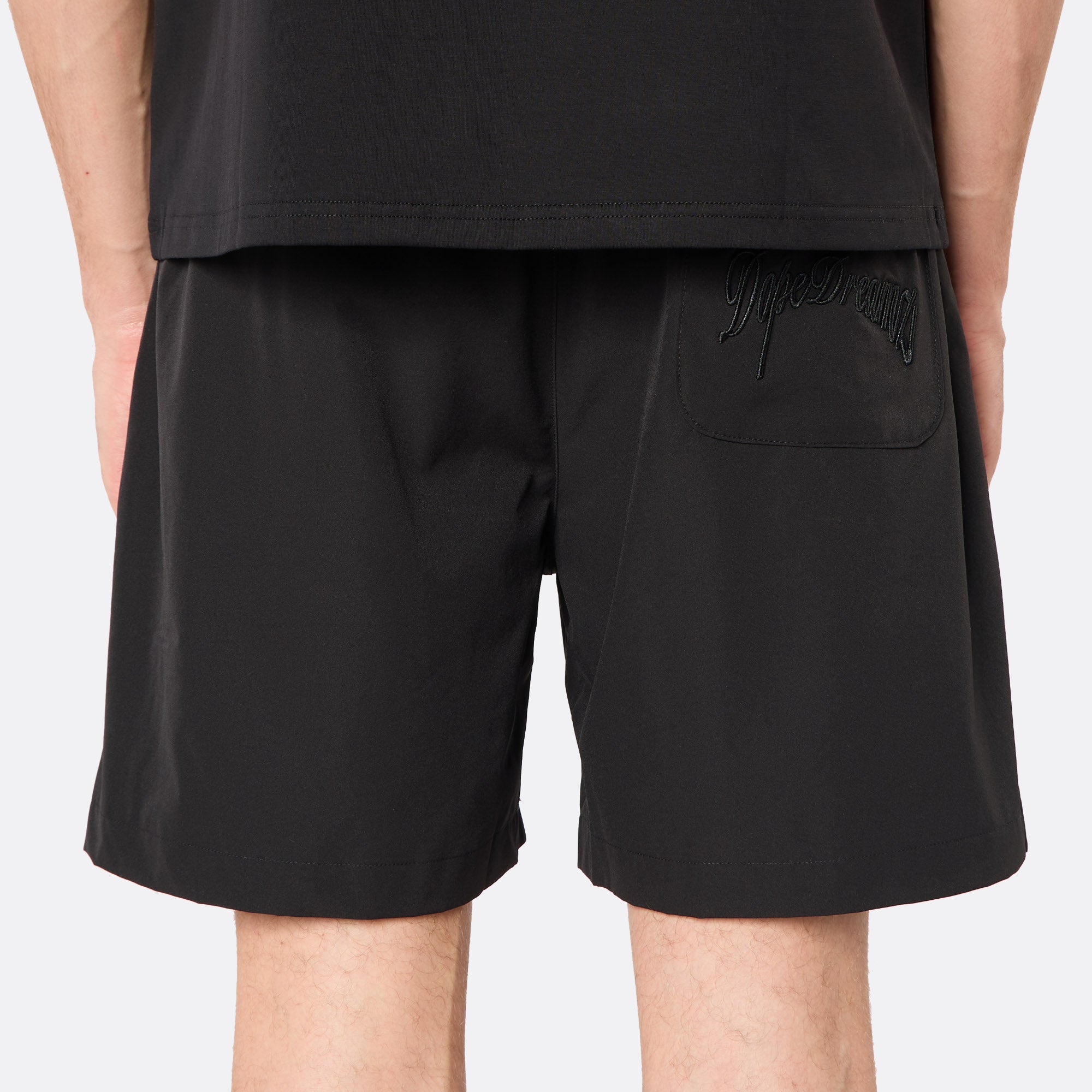 Rear view of the DopeDreamz Interlude Noir black shorts showcasing the tonal embroidered DopeDreamz script logo on the back pocket, finished with a tonal DDZ metal button closure.