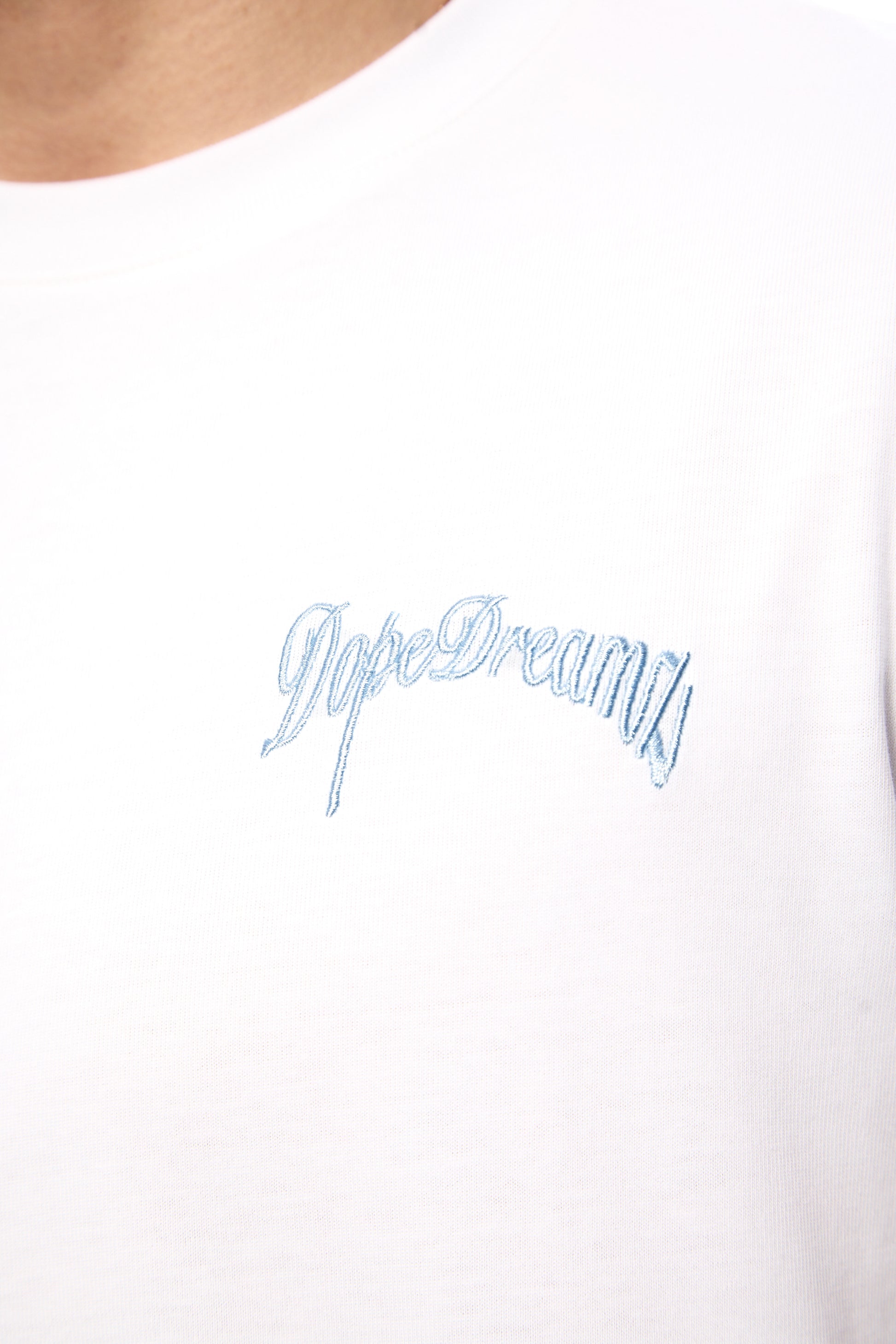 Close-up of blue 3D embroidered DopeDreamz logo on white t-shirt
