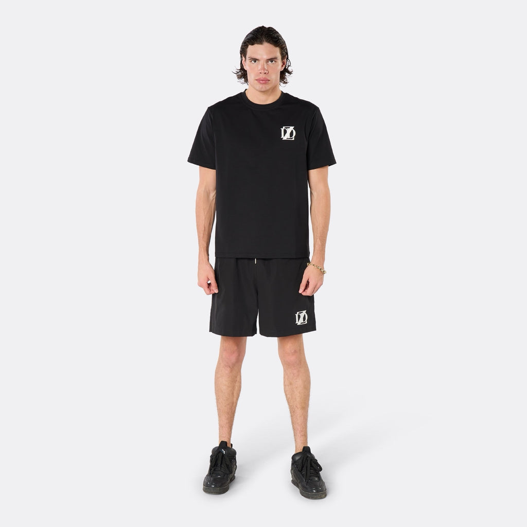 Male model wearing the DopeDreamz Interlude Noir black premium T-shirt with white DDZ chest logo and black shorts with white DDZ logo, front view.