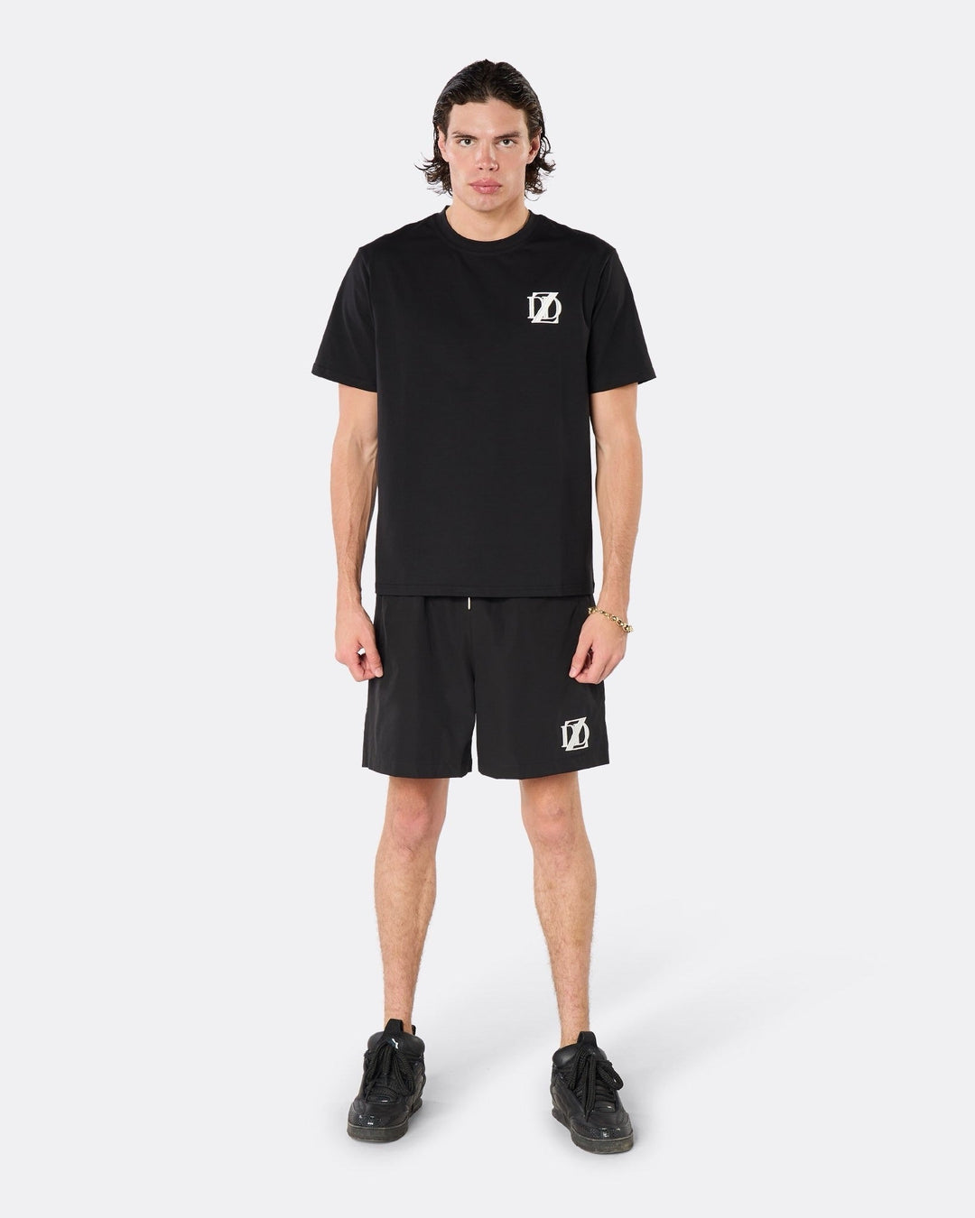 Male model wearing the DopeDreamz Interlude Noir black premium T-shirt with white DDZ chest logo and black shorts with white DDZ logo, front view.