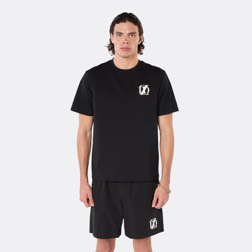 Male model wearing the DopeDreamz Interlude Noir black premium T-shirt with white DDZ chest logo and black shorts with white DDZ logo, close-up front view.