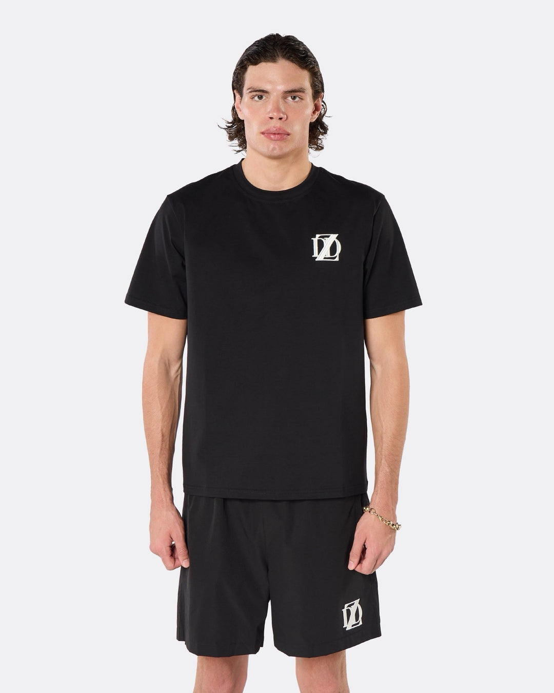 Male model wearing the DopeDreamz Interlude Noir black premium T-shirt with white DDZ chest logo and black shorts with white DDZ logo, close-up front view.