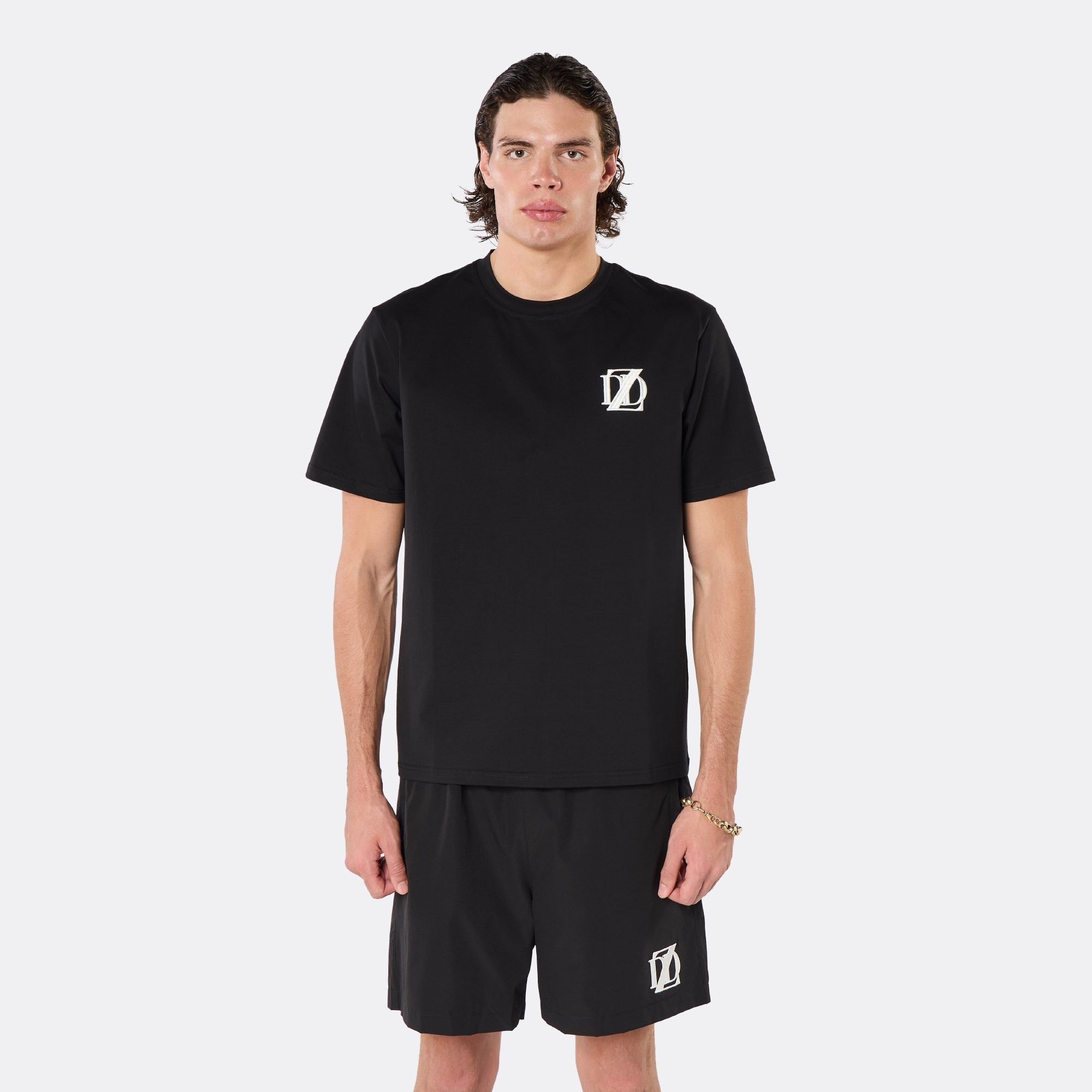 Male model wearing the DopeDreamz Interlude Noir black premium T-shirt with white DDZ chest logo and black shorts with white DDZ logo, close-up front view.