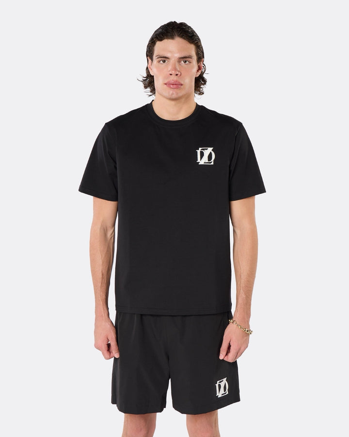 Male model wearing the DopeDreamz Interlude Noir black premium T-shirt with white DDZ chest logo and black shorts with white DDZ logo, close-up front view.
