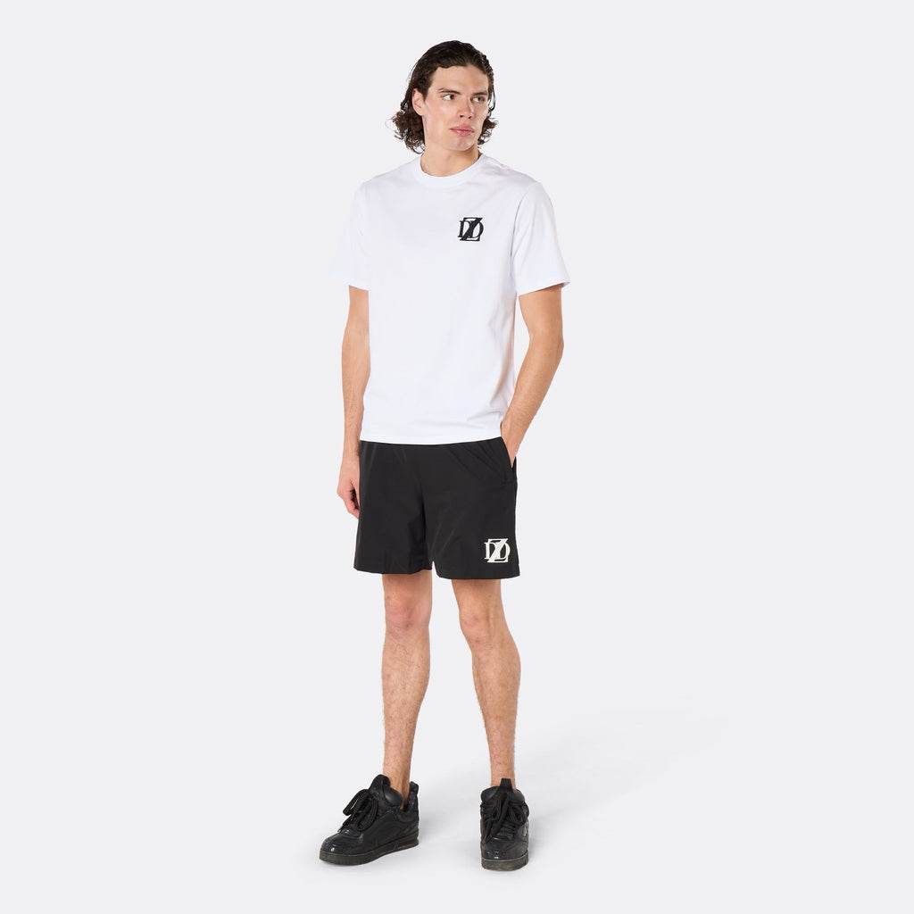 Male model wearing the DopeDreamz Interlude Noir white premium T-shirt with black DDZ chest logo and black shorts with white DDZ logo, three-quarter side view. 