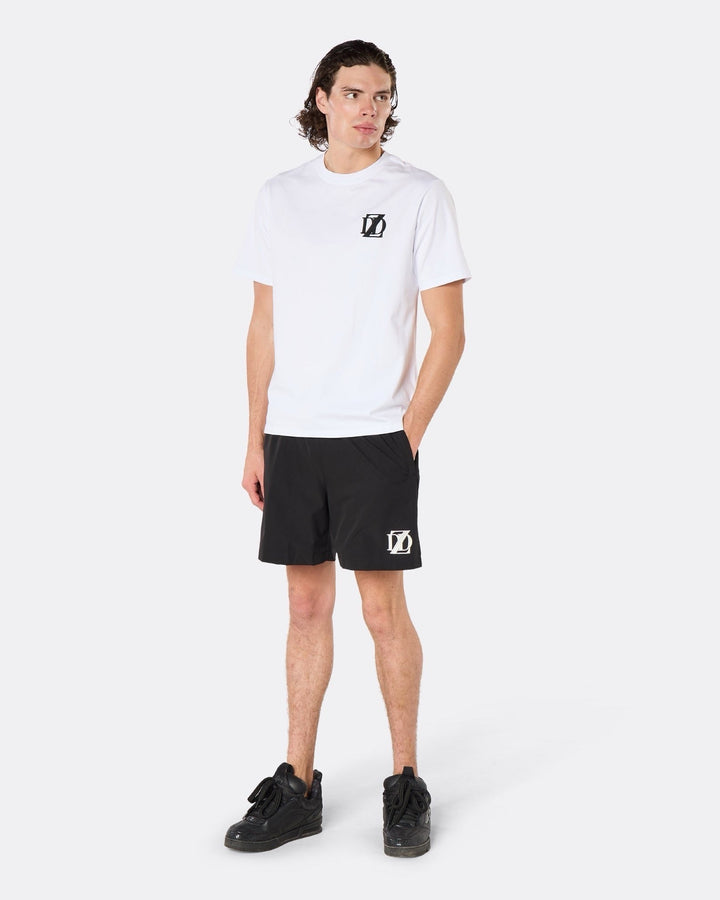 Male model wearing the DopeDreamz Interlude Noir white premium T-shirt with black DDZ chest logo and black shorts with white DDZ logo, three-quarter side view. 