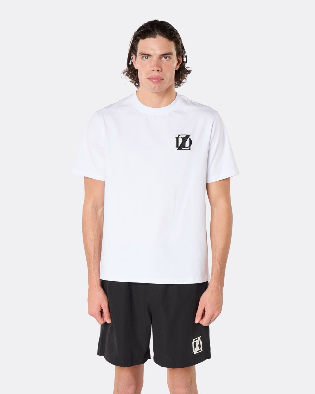 Male model wearing the DopeDreamz Interlude Noir white premium T-shirt with black DDZ chest logo and black shorts with white DDZ logo, close-up front view.