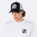 Three-quarter front view of a male model wearing the DopeDreamz Interlude Noir black and white trucker cap with white embroidered DDZ logo and white premium T-shirt with black embroidered DDZ chest logo.
