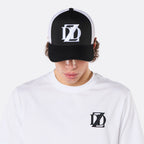 Close-up front view of a male model wearing the DopeDreamz Interlude Noir black and white trucker cap with white embroidered DDZ logo and the white premium T-shirt with black embroidered DDZ chest logo.