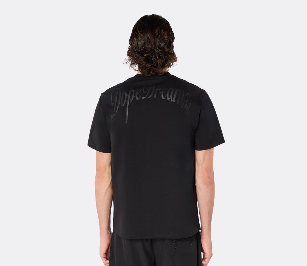 Male model wearing the DopeDreamz Interlude Noir black premium T-shirt with tonal black DopeDreamz back graphic and black shorts with tonal black DopeDreamz logo, back view.