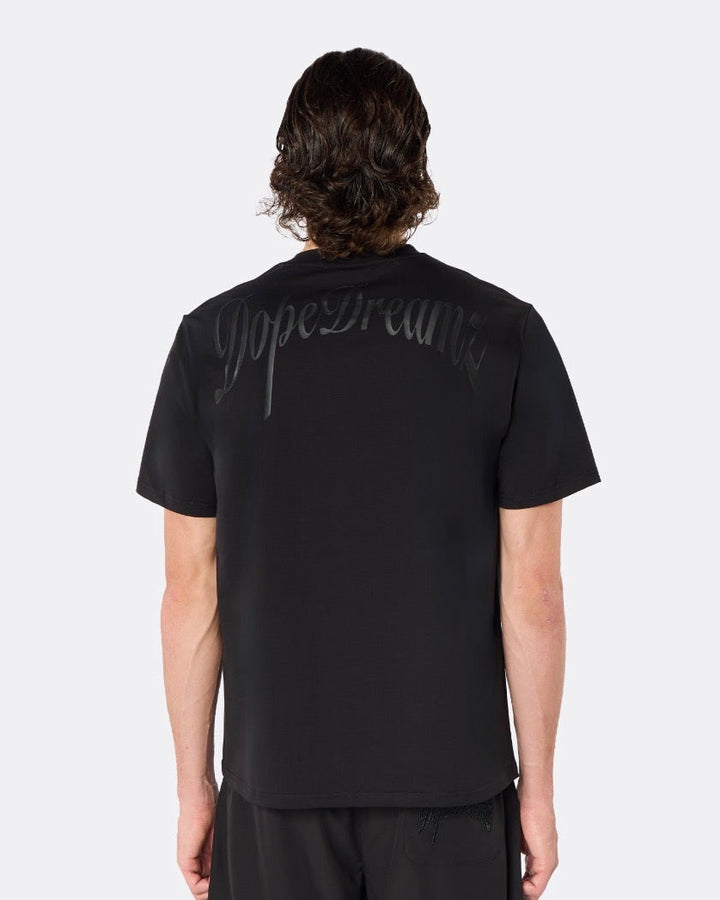 Male model wearing the DopeDreamz Interlude Noir black premium T-shirt with tonal black DopeDreamz back graphic and black shorts with tonal black DopeDreamz logo, back view.