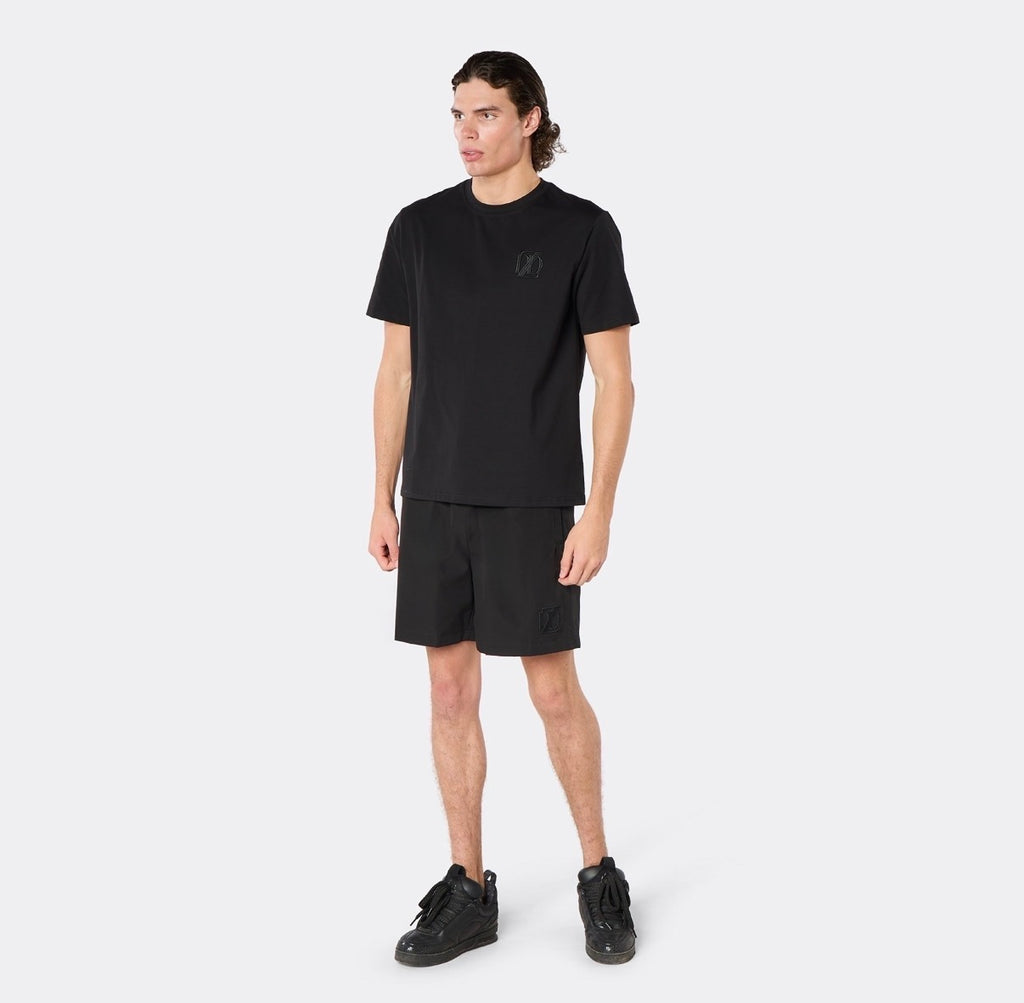 Male model wearing the DopeDreamz Interlude Noir black premium T-shirt with tonal black DDZ chest logo and black shorts with tonal black DDZ logo, three-quarter front view.