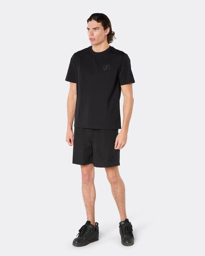 Male model wearing the DopeDreamz Interlude Noir black premium T-shirt with tonal black DDZ chest logo and black shorts with tonal black DDZ logo, three-quarter front view.