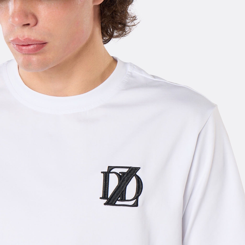 Close-up of a male model wearing the DopeDreamz Interlude Noir white premium T-shirt with black embroidered DDZ chest logo.