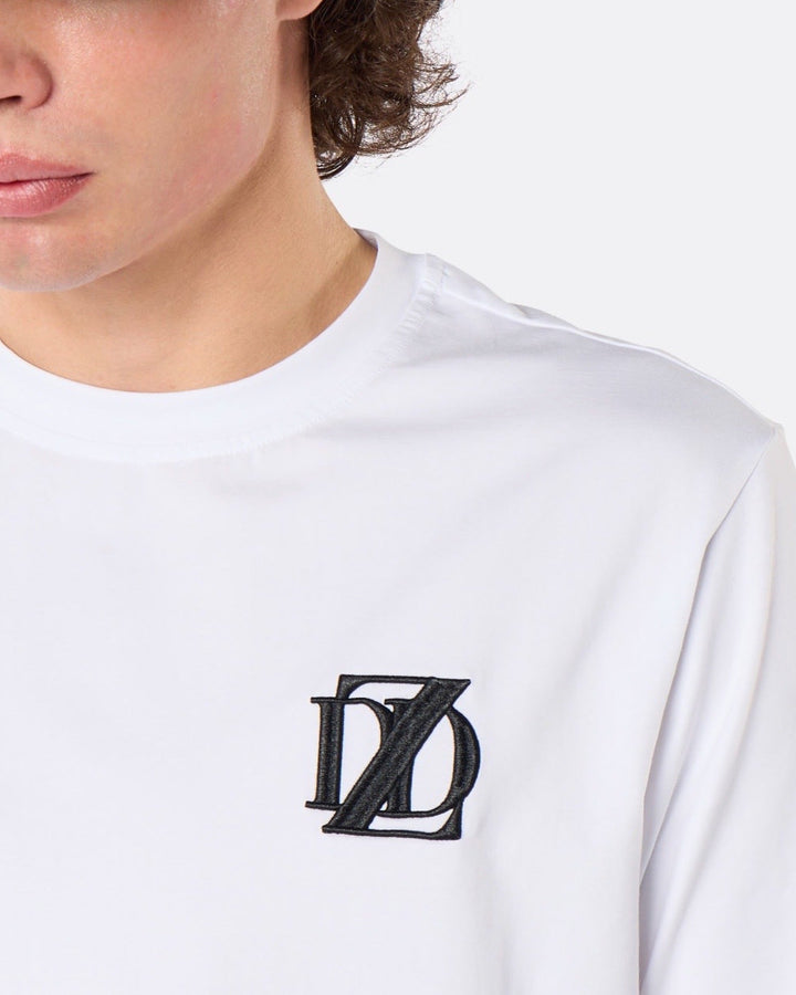 Close-up of a male model wearing the DopeDreamz Interlude Noir white premium T-shirt with black embroidered DDZ chest logo.