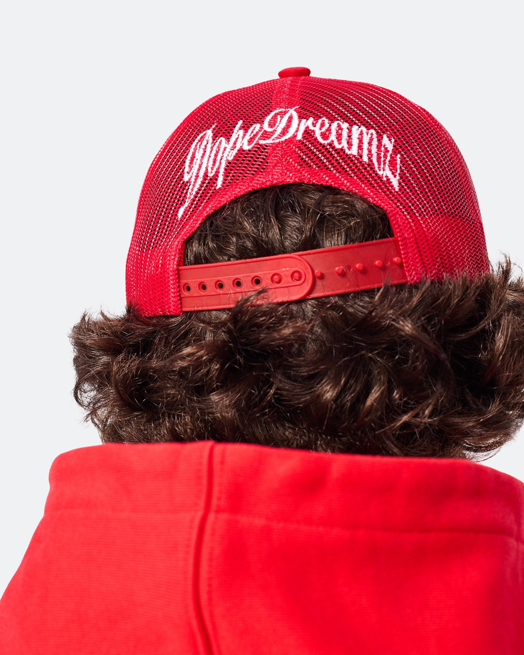 Back view of red DopeDreamz trucker cap with white embroidered logo and adjustable strap

