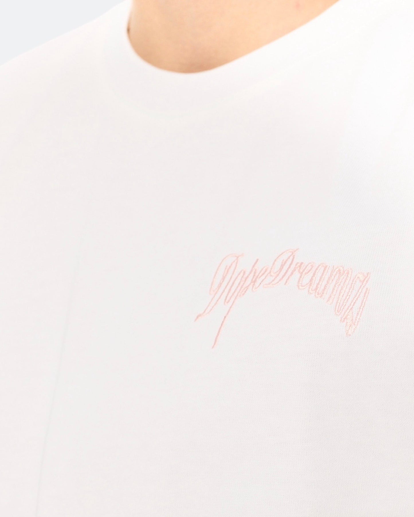 Close-up of baby pink 3D embroidered DopeDreamz logo on white t-shirt
