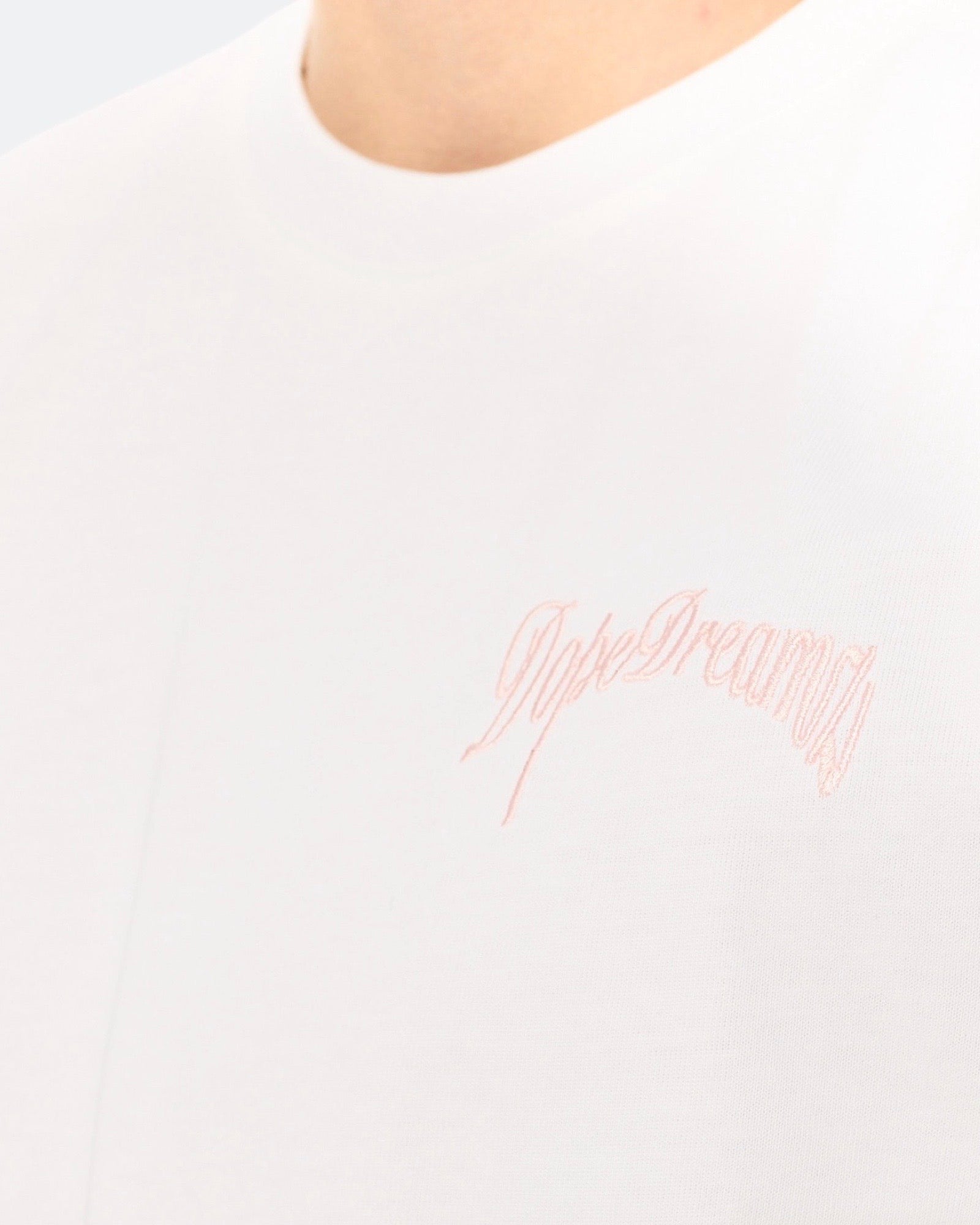 Close-up of baby pink 3D embroidered DopeDreamz logo on white t-shirt
